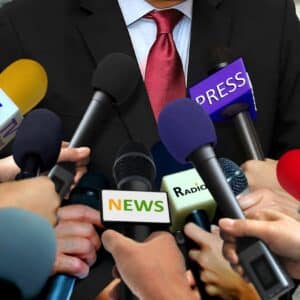 An image of a man in a suit being interviewed by several news reporters.