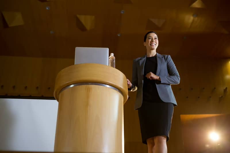 Executive business leader delivering a keynote presentation to an audience, demonstrating thought leadership and the ROI of personal branding.