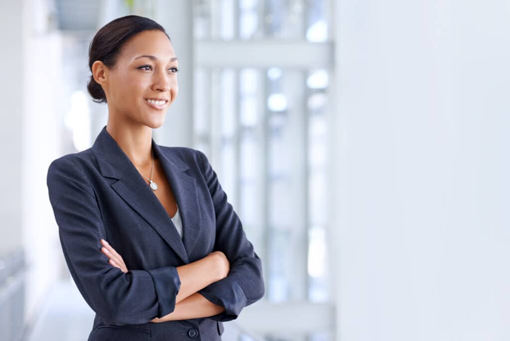 Confident businesswoman wearing a navy blazer with arms crossed in a modern office, representing professional confidence and personal branding.